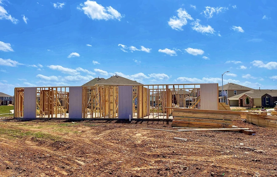 Wood-framed new home under construction on a dirt lot beneath a blue sky