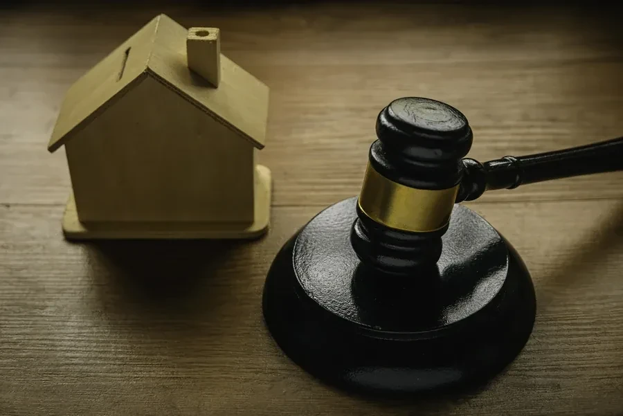 Small wooden house model beside a judge's gavel representing a lawsuit against a property