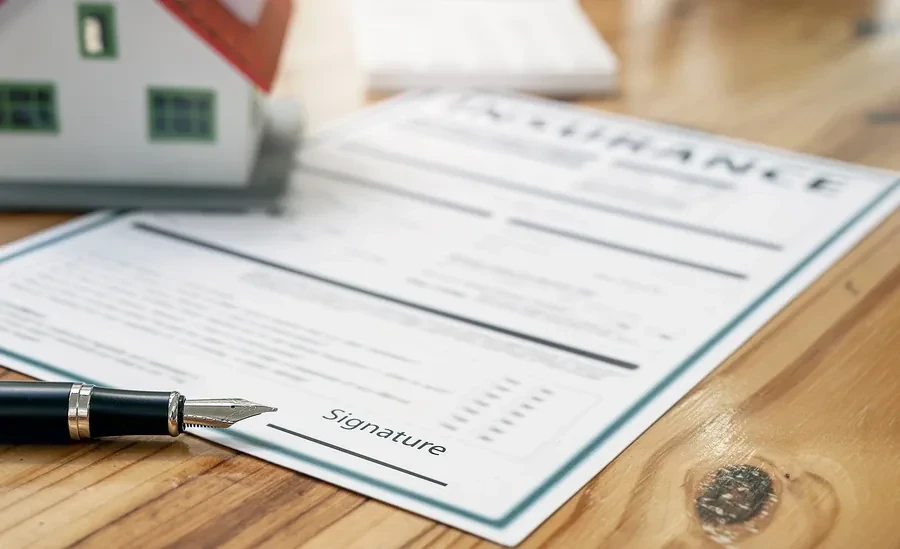 Insurance policy form with a fountain pen and small house model on a wood desk